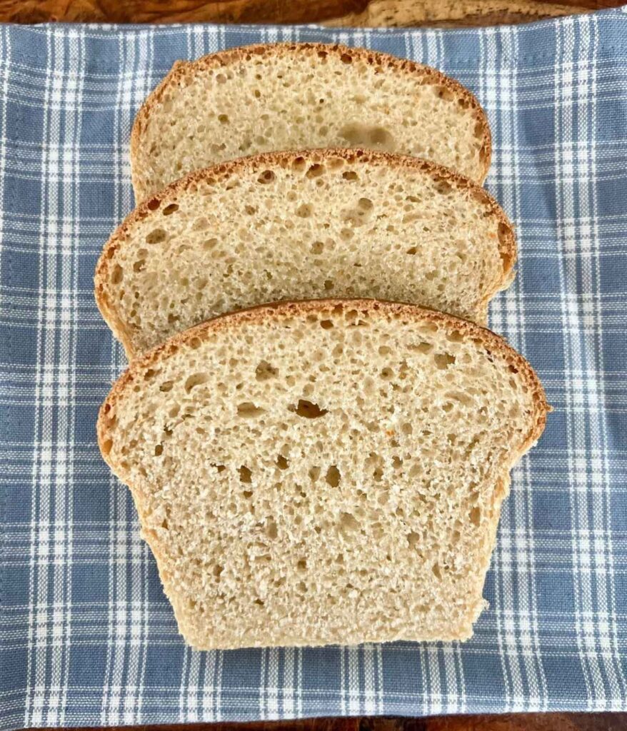 Three slices of honey wheat sourdough sandwich bread on a blue checkered napkin.