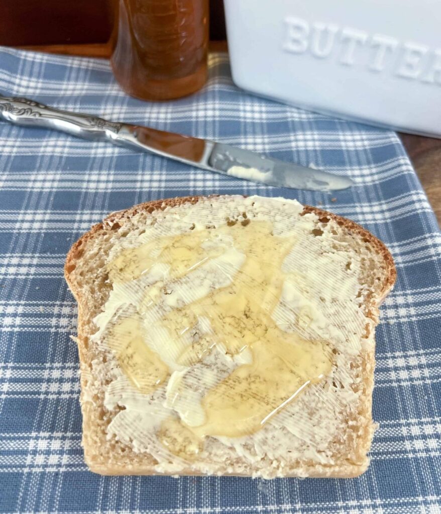 A slice of honey wheat sourdough sandwich bread with butter and honey on it.