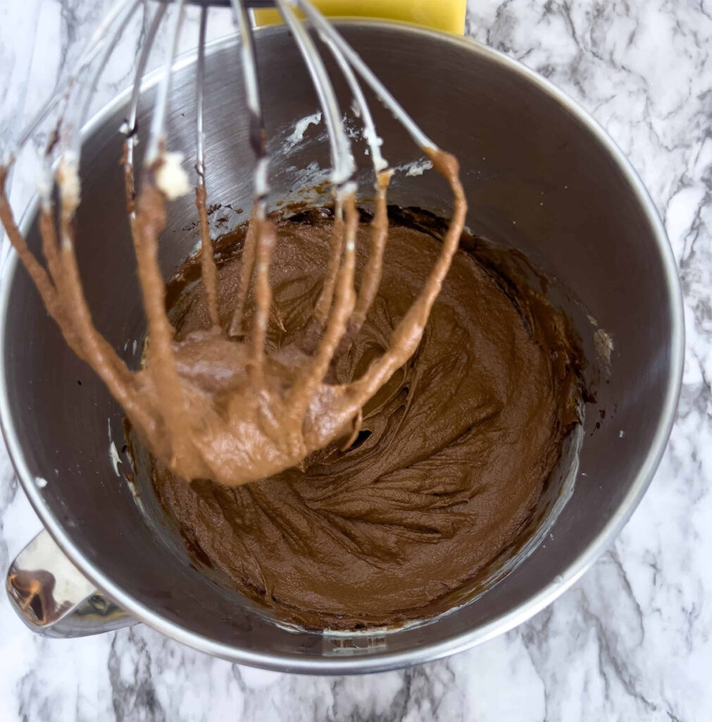 A mixture of melted chocolate, sugar, butter, and eggs in a stand mixer.