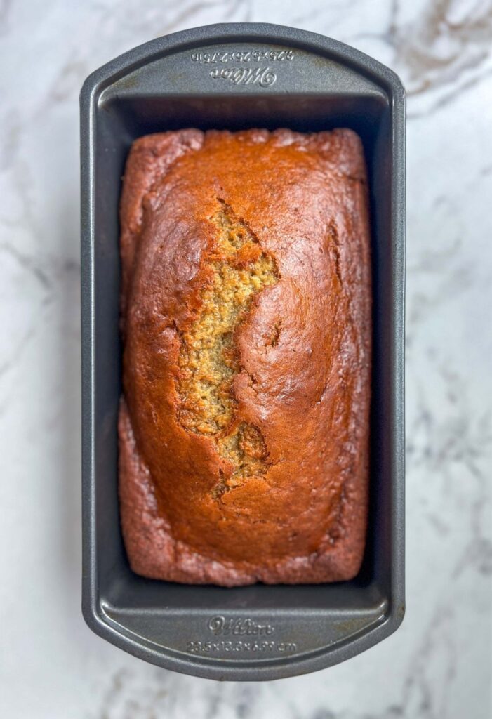 A loaf of no oil banana bread in a metal loaf pan on a marble countertop.