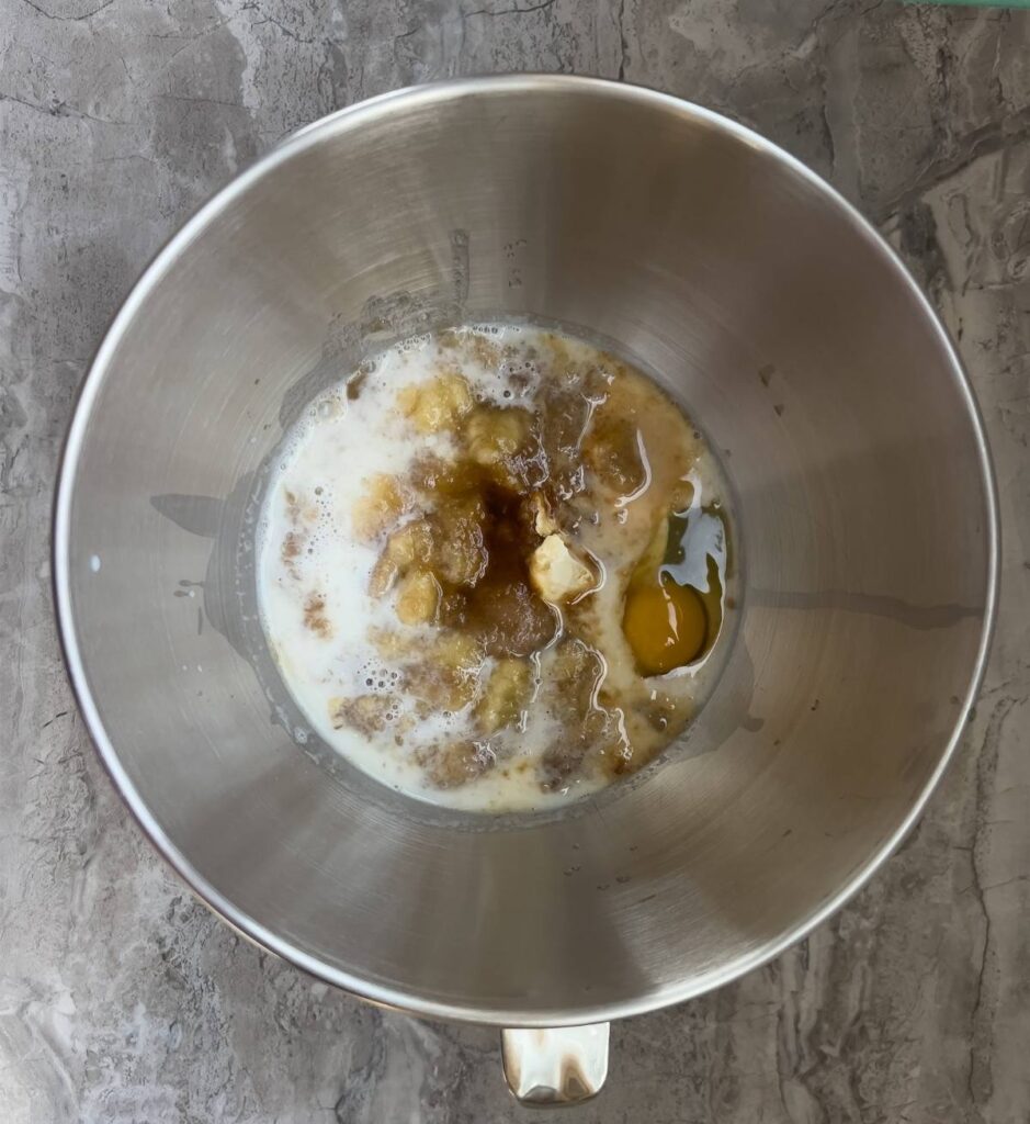 A mixture of wet ingredients including eggs, milk, and sour cream in a stainless steel bowl.