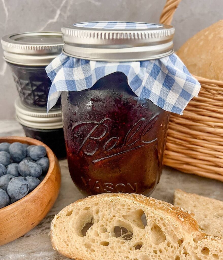 Easy blueberry preserves in a mason jar with a blue checkered fabric lid. 