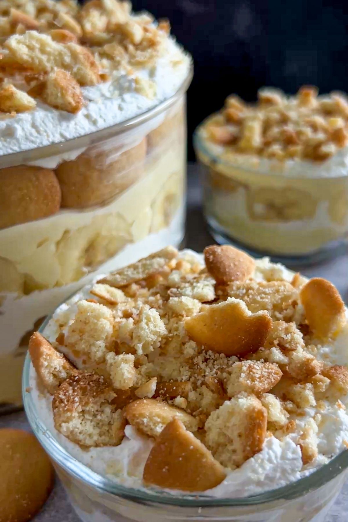A cup of the best southern banana pudding with crushed vanilla wafers as a topping. More pudding is in the background.