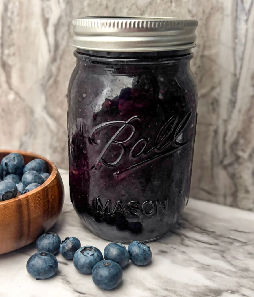 Easy blueberry bourbon preserves (no pectin) in a mason jar next to blueberries.