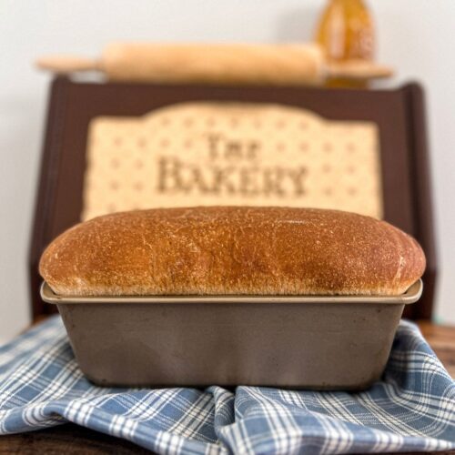 A loaf of honey wheat sourdough sandwich bread in front of a brown bread box.