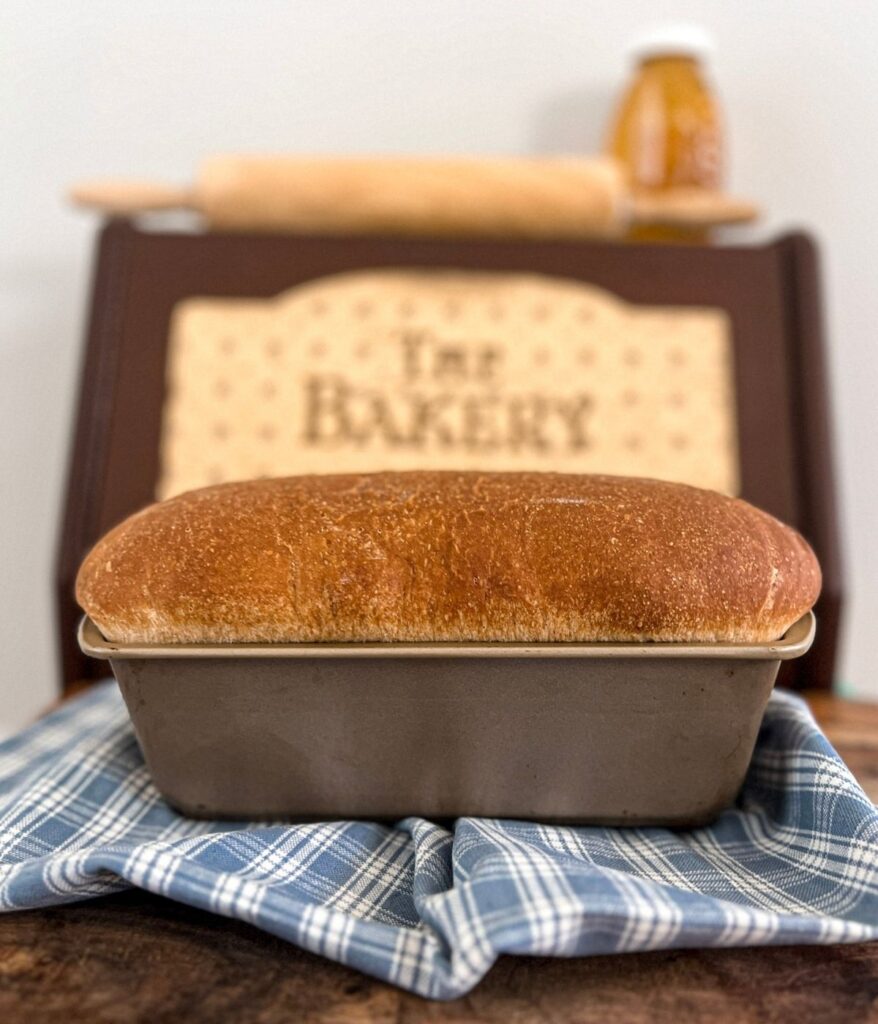 A loaf of honey wheat sourdough sandwich bread in front of a brown bread box.