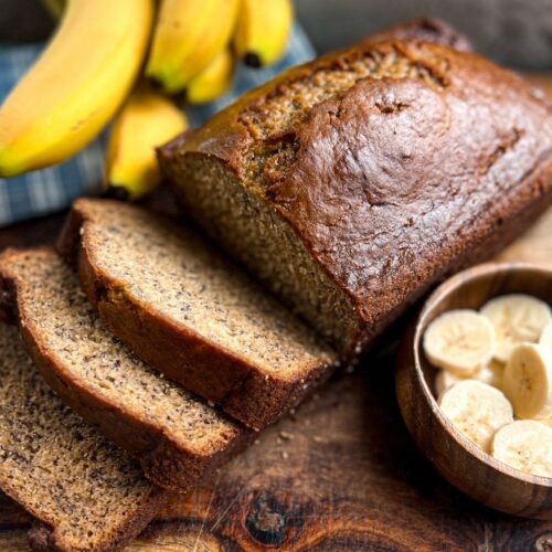 Slices of no oil banana bread next to a bowl of banana slices and whole bananas in the background.