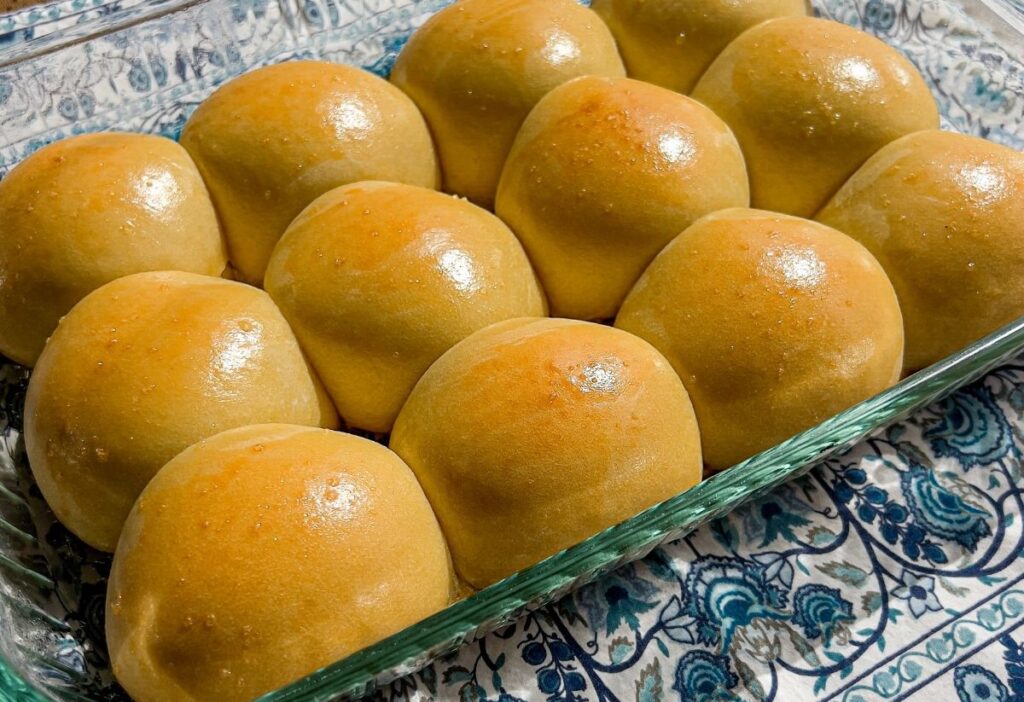 A glass casserole dish filled with twelve sourdough Hawaiian rolls fresh out of the oven.