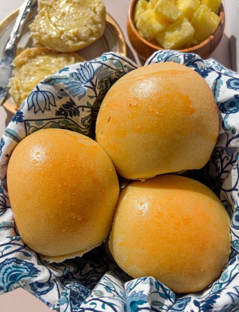 A closeup of three sourdough Hawaiian rolls resting in a basket lined with a blue and white cloth napkin.
