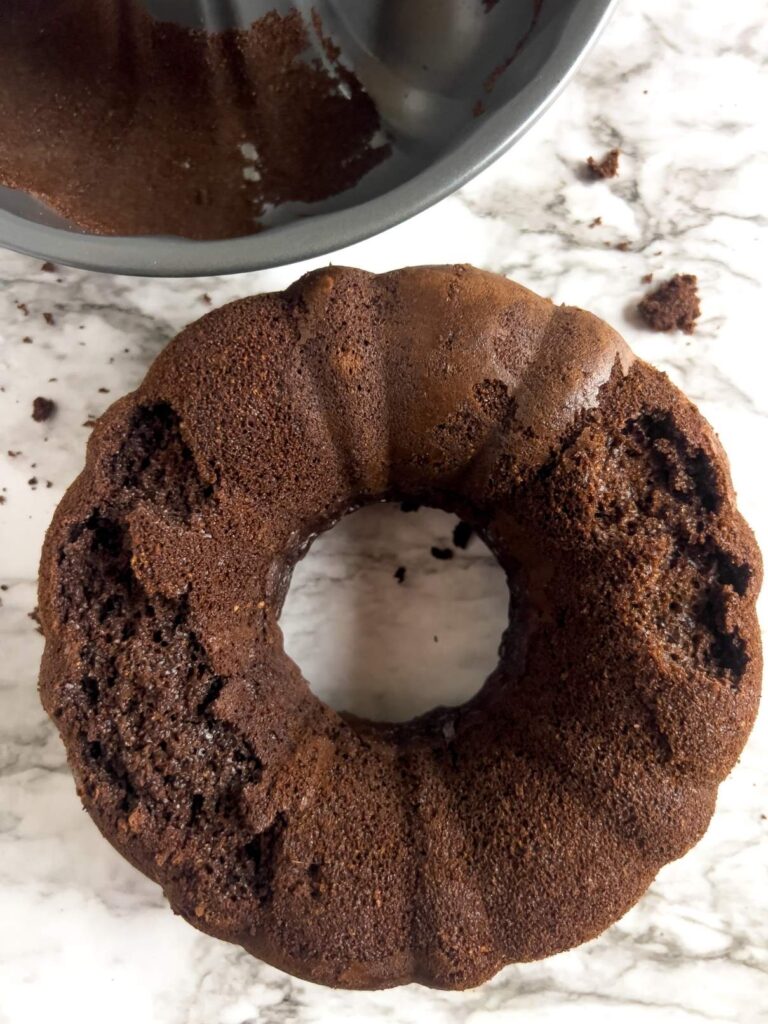 A picture of a bundt cake that is broken because some of it stuck to the pan. The pan is in the background.
