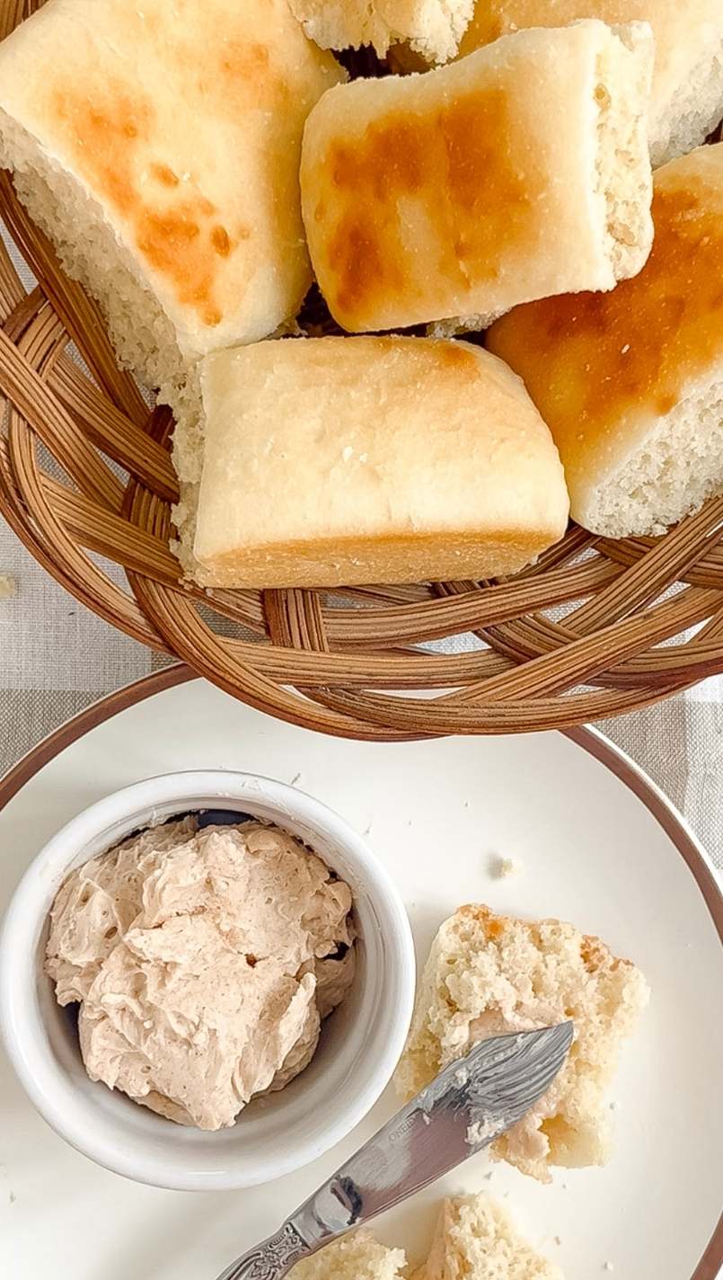 A basket of easy one day sourdough Texas Roadhouse rolls on a tan and white checkered background with a plate of honey cinnamon butter underneath. 