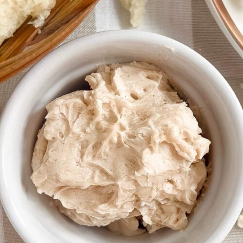 A small white dish of homemade honey cinnamon butter on a tan and white checkered background.
