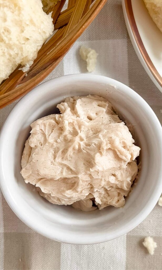 A small white dish of homemade honey cinnamon butter on a tan and white checkered background.