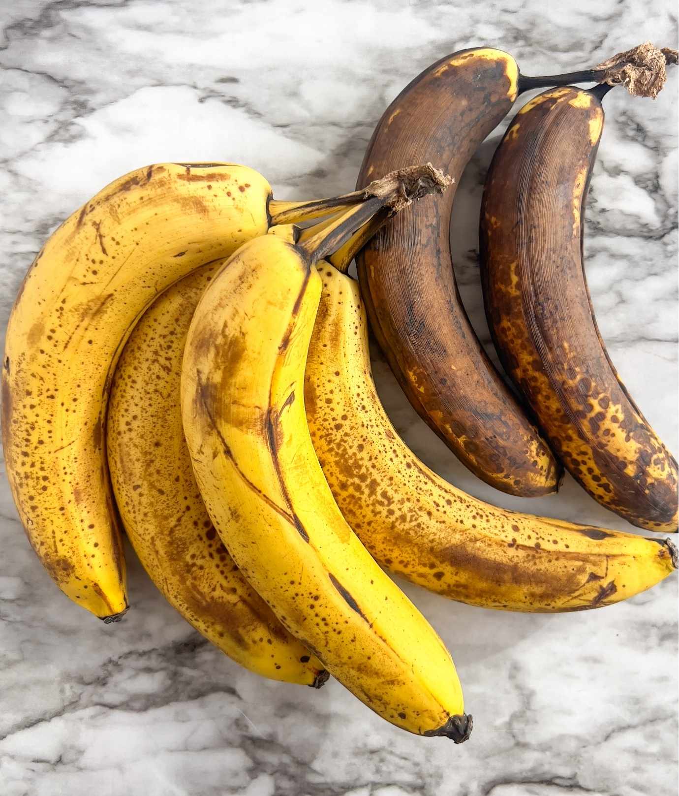 An assortment of overripe and black bananas on a white marble countertop.