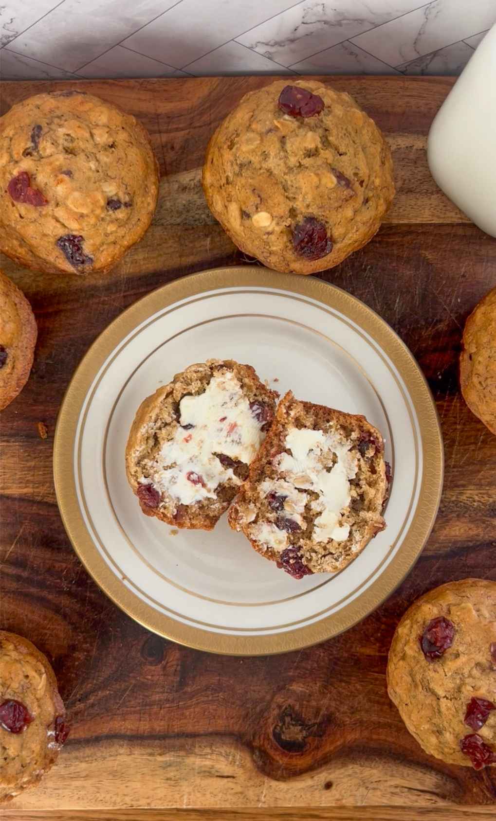 Whole Wheat Cranberry Banana Oatmeal Muffins surrounded by a muffin cut in half with butter spread on it. 