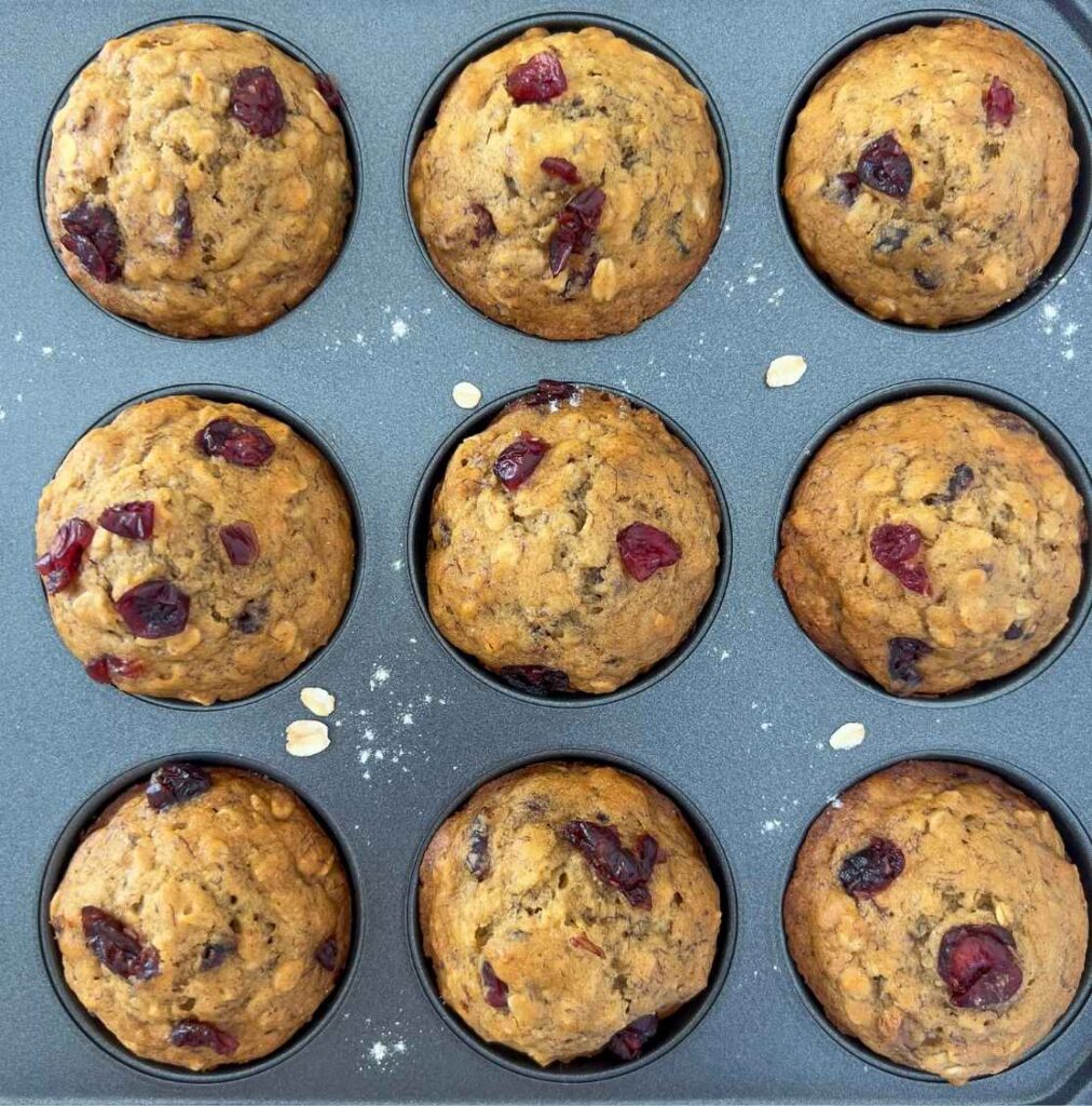 Nine Whole Wheat Cranberry Banana Oatmeal Muffins in a silver muffin pan. 