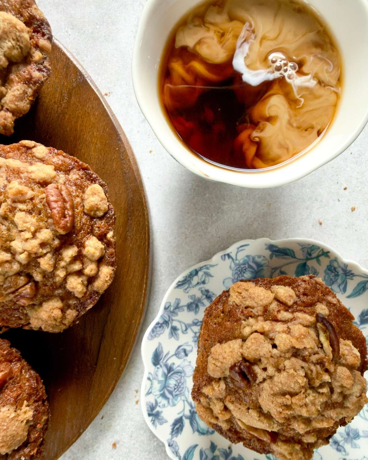 A bakery style banana nut muffin on a plate next to a cup of coffee and more muffins on a wooden board.