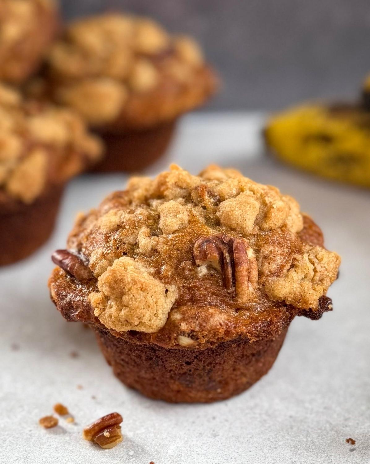 A bakery style banana nut muffin in front of muffins and bananas.