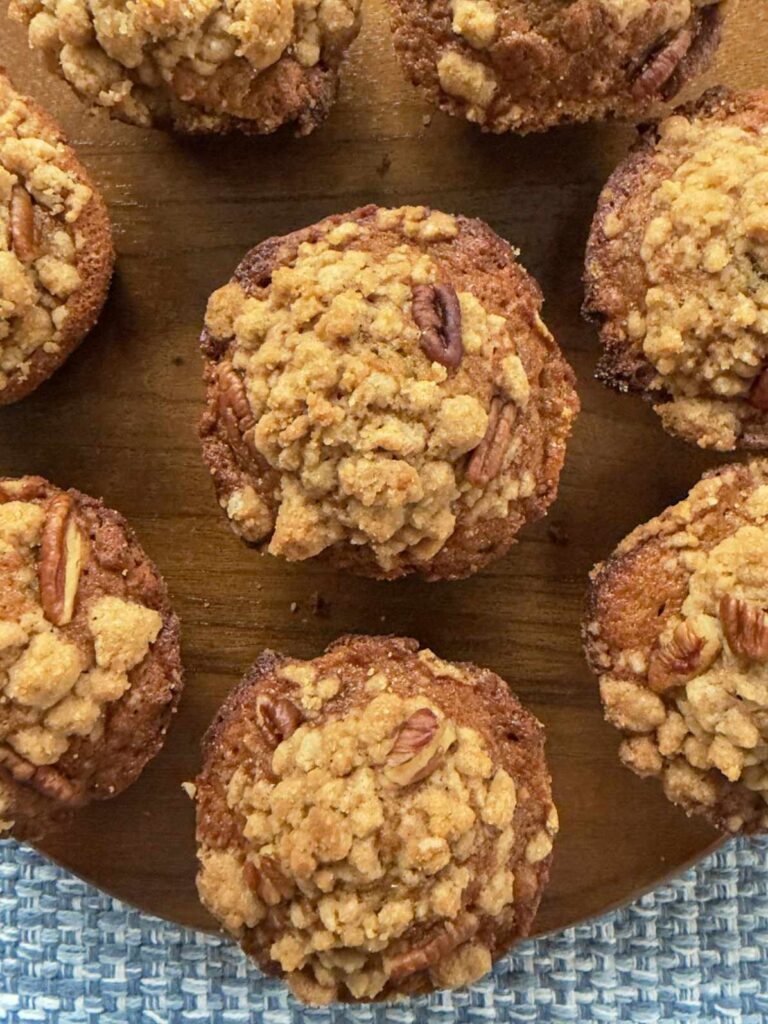 Six bakery style banana nut muffins on a wooden board.